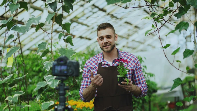 Man holding a potted plant in a greenhouse.